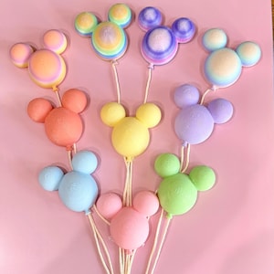 May include: A collection of nine balloon-shaped ornaments, each featuring a central circular body with two smaller circular ears. The balloons display various solid and gradient pastel colors, including pink, blue, yellow, green, and purple, and are attached to thin white strings.