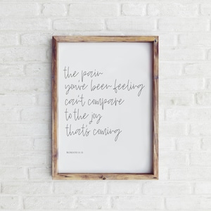 May include: A framed print with a white background and black text that reads "The pain you've been feeling can't compare to the joy that's coming."  The text is in a handwritten font.  The bottom of the print reads "Romans 8:18".