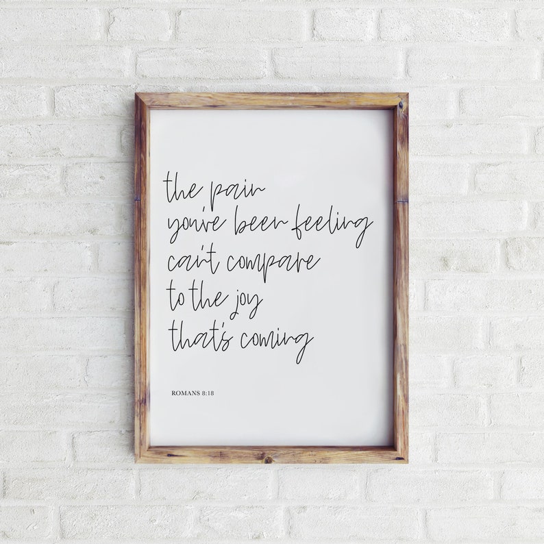 May include: A framed print with a white background and black text that reads "The pain you've been feeling can't compare to the joy that's coming."  The text is in a handwritten font.  The bottom of the print reads "Romans 8:18".