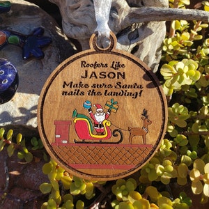 May include: A round wooden ornament with a Santa Claus illustration. The ornament reads "Roofers Like JASON Make sure Santa nails the landing!"