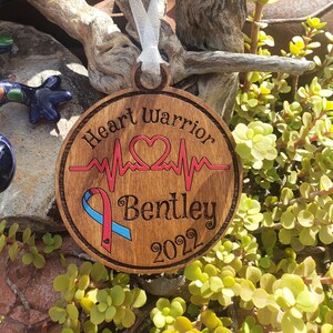 Può includere: Ciondolo in legno a forma di cuore di guerriero con un cuore rosso, un nastro blu e rosso e il testo "Heart Warrior" e "Bentley 2022".