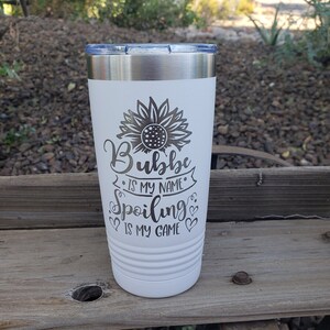 May include: White stainless steel tumbler with a black sunflower design and the text "Bubba is my name, spoiling is my game".