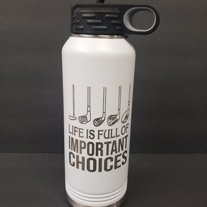 Puede incluir: Botella de agua de acero inoxidable blanca con tapa y asa negras. La botella tiene un gráfico de palos de golf y el texto "Life is full of important choices".