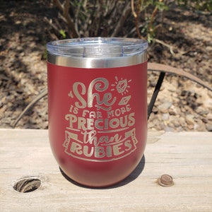 Peut inclure: Un gobelet en acier inoxydable rouge avec une inscription dorée qui dit "Elle est bien plus précieuse que les rubis".