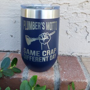 Könnte beinhalten: Ein marineblauer Edelstahlbecher mit silbernem Deckel. Der Becher hat eine silberne Aufschrift mit dem Text "Plumber's Motto: Same Crap Different Day".