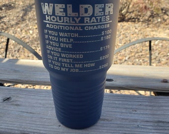 May include: A blue stainless steel tumbler with a silver lid. The tumbler has the words "Welder Hourly Rates" and a list of additional charges for services.