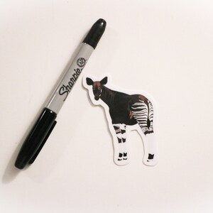May include: A black and white okapi sticker with a black Sharpie marker on a white background.