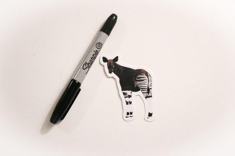 May include: A black and white okapi sticker with a black Sharpie marker on a white background.