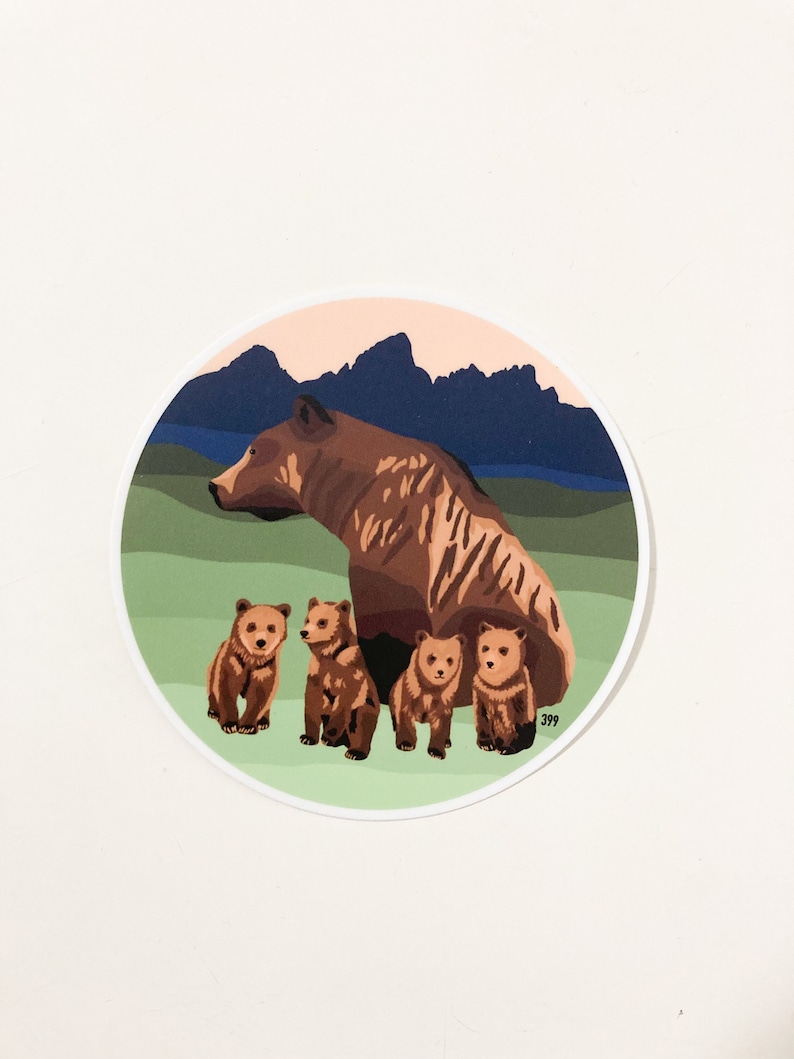 May include: A brown bear with four cubs in a circular sticker. The background is a green field with a blue mountain range in the distance. The sky is a light pink color.