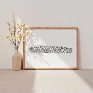 May include: A framed black and white line drawing of the silhouette of the Green Mountains in Vermont. The print is in a light wood frame and is sitting on a light beige surface.