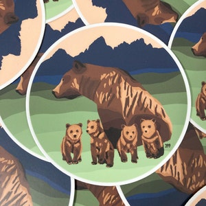 May include: A brown bear with four cubs stands in a green field with a blue mountain range in the background. The bear and cubs are all facing the right side of the image. The image is a sticker with a white border and the number 399 printed in the bottom right corner.