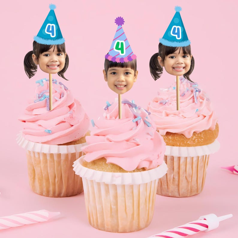 May include: Three cupcakes with pink frosting and a face cutout on a stick, each wearing a party hat with the number 4. The cupcakes sit on a pink background with candles.