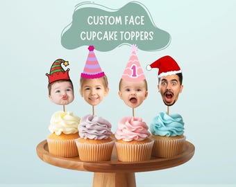 May include: Four cupcakes with white, lavender, pink, and light blue frosting, each topped with a custom face cutout on a stick. The faces wear a green and red elf hat, a striped party hat, a pink party hat with the number 1, and a red Santa hat.