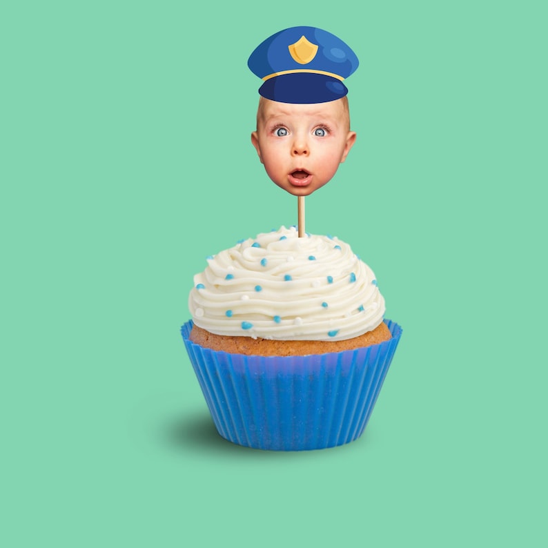 May include: A cupcake with white frosting and blue sprinkles, in a blue liner. A baby's face wearing a blue police hat is attached to a stick and placed on top of the cupcake. The background is a solid teal color.