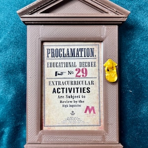 May include: A brown wooden frame with a sign that reads "PROCLAMATION. EDUCATIONAL DECREE No. 29 EXTRACURRICULAR ACTIVITIES Are Subject to Review by the High Inquisitor" with a gold door handle.