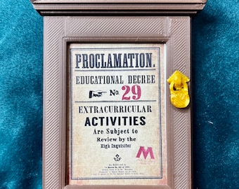 May include: A brown wooden frame with a sign that reads "PROCLAMATION. EDUCATIONAL DECREE No. 29 EXTRACURRICULAR ACTIVITIES Are Subject to Review by the High Inquisitor" with a gold door handle.