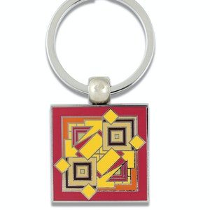 May include: A red, yellow, and brown geometric design on a metal keychain. The design is made up of squares and diamonds.