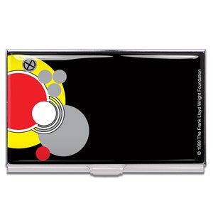 May include: A rectangular business card holder with a black background and a colorful abstract design. The design includes red, yellow, white, and gray circles. The holder has a silver metal frame and the text "© 1999 The Frank Lloyd Wright Foundation".