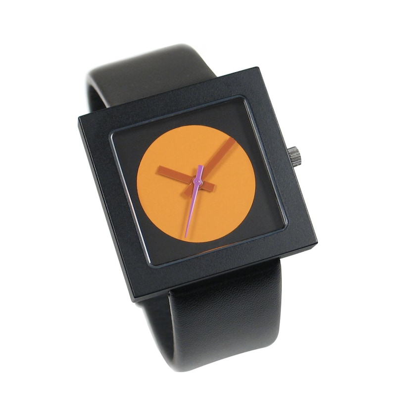 K&ouml;nnte beinhalten: Eine schwarze quadratische Uhr mit einem schwarzen Lederarmband. Das Zifferblatt der Uhr ist ein leuchtend orangefarbener Kreis mit schwarzen Zeigern und einem violetten Sekundenzeiger.