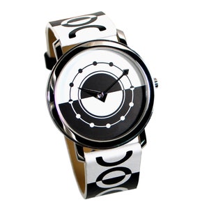 May include: A black and white wristwatch with a circular face and a silver band. The watch face has a black and white design with a circle of dots around the edge.