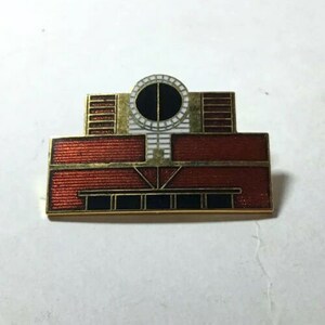 May include: A gold-toned enamel pin featuring a red and white stylized building with a round window. The pin is a representation of a famous architectural structure.