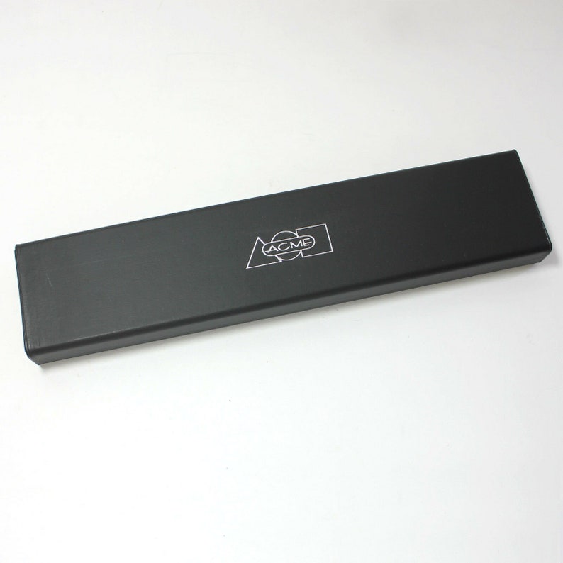 May include: A black rectangular box with the word "ACME" printed in white on the top. The box is made of a smooth, hard material.