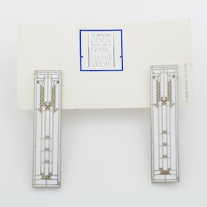 May include: A pair of white and gold enamel earrings with a geometric design. The earrings are inspired by the work of Frank Lloyd Wright. The earrings are made by Acme Studios.