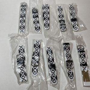 May include: A collection of 11 black and white watch bands with a circle pattern. The bands are packaged individually in clear plastic bags.