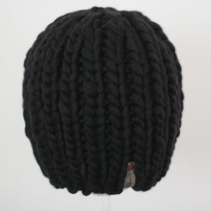 May include: A black, chunky knit beanie hat. The hat is made of thick yarn, with a ribbed texture. A small tag is sewn on the bottom edge. This warm hat is perfect for cold weather.