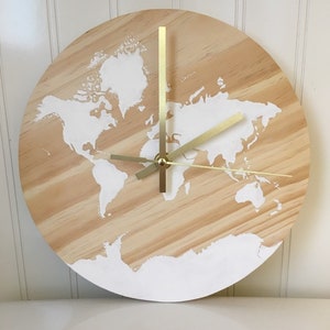 May include: A round wooden clock with a white painted world map design and gold-colored hands.