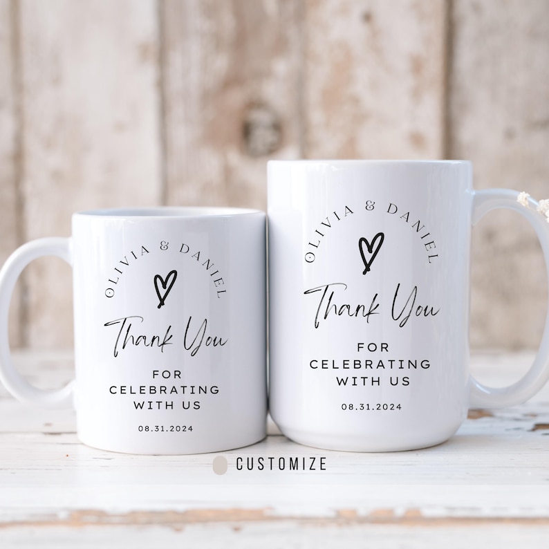 May include: Two white ceramic mugs with black text and a heart design. The text on the mugs reads "Olivia & Daniel" and "Thank You for Celebrating with Us 08.31.2024".