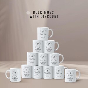 May include: A stack of 10 white ceramic mugs with black text that reads "Thank You for Celebrating with Us". The mugs are arranged in a pyramid shape. The text is in a simple, modern font.