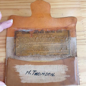 Può includere: Una custodia in pelle marrone con un regolo calcolatore in ottone all'interno. La custodia presenta il testo "HUDSON HORSE POWER COMPUTING SCALE" e "H. THOMSON" sul davanti. Il regolo calcolatore viene utilizzato per calcolare la potenza di un motore.