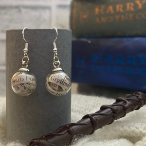 May include: Silver earrings with glass orbs filled with paper scraps from Harry Potter books. The paper scraps include the words "Gryffindor" and "Hogwarts Express".
