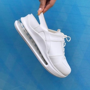 May include: White leather sneaker with a clear, bubble-like sole. The shoe has a lace-up closure and a strap at the back.