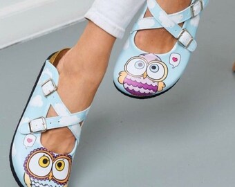 May include: A pair of blue and white slip-on shoes with an owl design. The shoes have white straps with buckles and a heart design.
