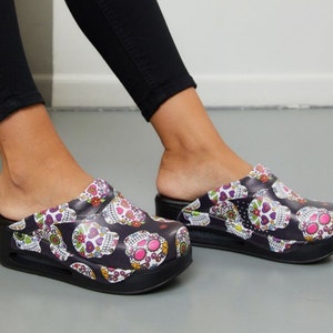 May include: Black clogs with a white platform sole and a colorful sugar skull print.