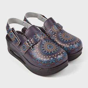 May include: A pair of dark purple clogs with a decorative mandala pattern in blue and orange. The clogs have a black sole and a strap that goes around the ankle. The clogs have a platform heel.