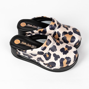 May include: A pair of black and white leopard print clogs with a black platform sole. The clogs have a black leather strap across the top and the text "Textil Sabo" is printed on the insole.
