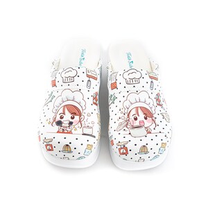 May include: White clogs with a cartoon chef design. The chef is wearing a white hat and holding a pot. The clogs have a black polka dot pattern and feature other kitchen-themed illustrations.