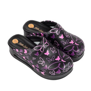 May include: A pair of black clogs with a purple butterfly print. The clogs have a platform sole and are made of a soft, comfortable material. The text "Textile Sabo" is printed on the inside of the clogs.