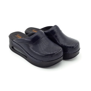 Può includere: Un paio di zoccoli blu navy con un design traforato e una suola spessa nera. Gli zoccoli hanno una punta arrotondata e un design slip-on.