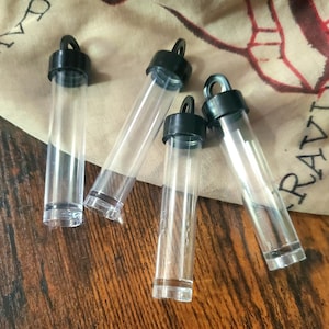 May include: Four clear plastic tubes with black lids and a loop at the top. The tubes are lying on a wooden surface.