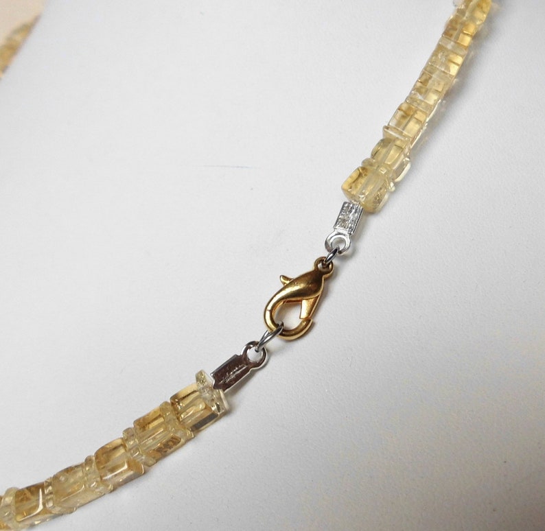 May include: A gold necklace with a clasp made of silver metal. The necklace is made of small, square-shaped, light brown stones.