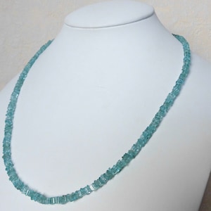 Op de afbeelding: Een lichtblauwe edelsteenketting gemaakt van vierkante kralen. De ketting wordt getoond op een witte mannequinbuste.