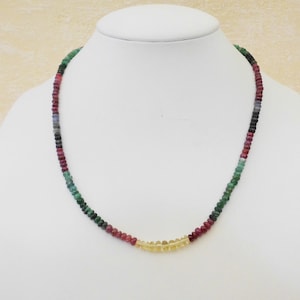 May include: A multi-colored gemstone necklace with green, red, blue, and yellow beads. The necklace is made of small, round beads and is strung on a thin chain.