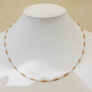 May include: A delicate necklace made with small white and brown beads. The necklace is displayed on a white mannequin bust.
