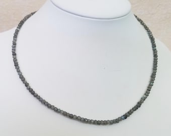 May include: A delicate necklace composed of small, faceted gray beads. The beads are strung together to form a choker-style necklace. The necklace is displayed on a white mannequin bust, showcasing its design and shape.
