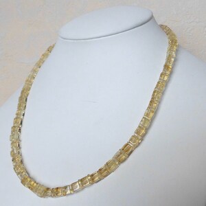 May include: A gold necklace made of square-shaped beads. The necklace is on a white mannequin.