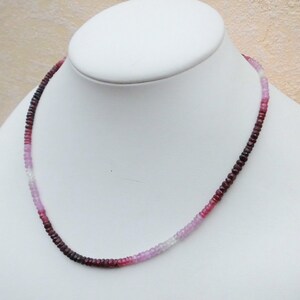 May include: A necklace made of small, faceted gemstones. The beads are graduated in size, with the largest beads at the bottom of the necklace. The beads are a mix of pink, red, and purple.
